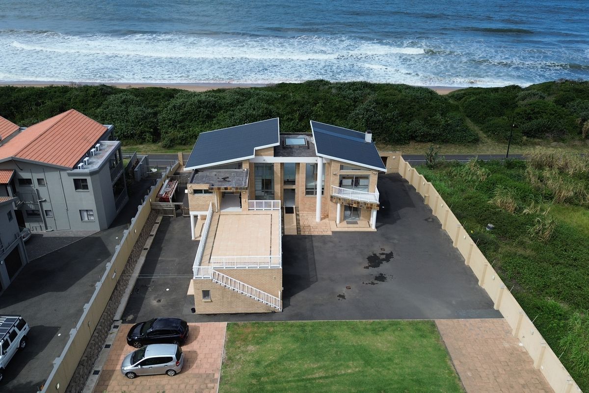 Aerial view of a beachfront property featuring a multi-level design, paved driveway, and direct access to the coastline.