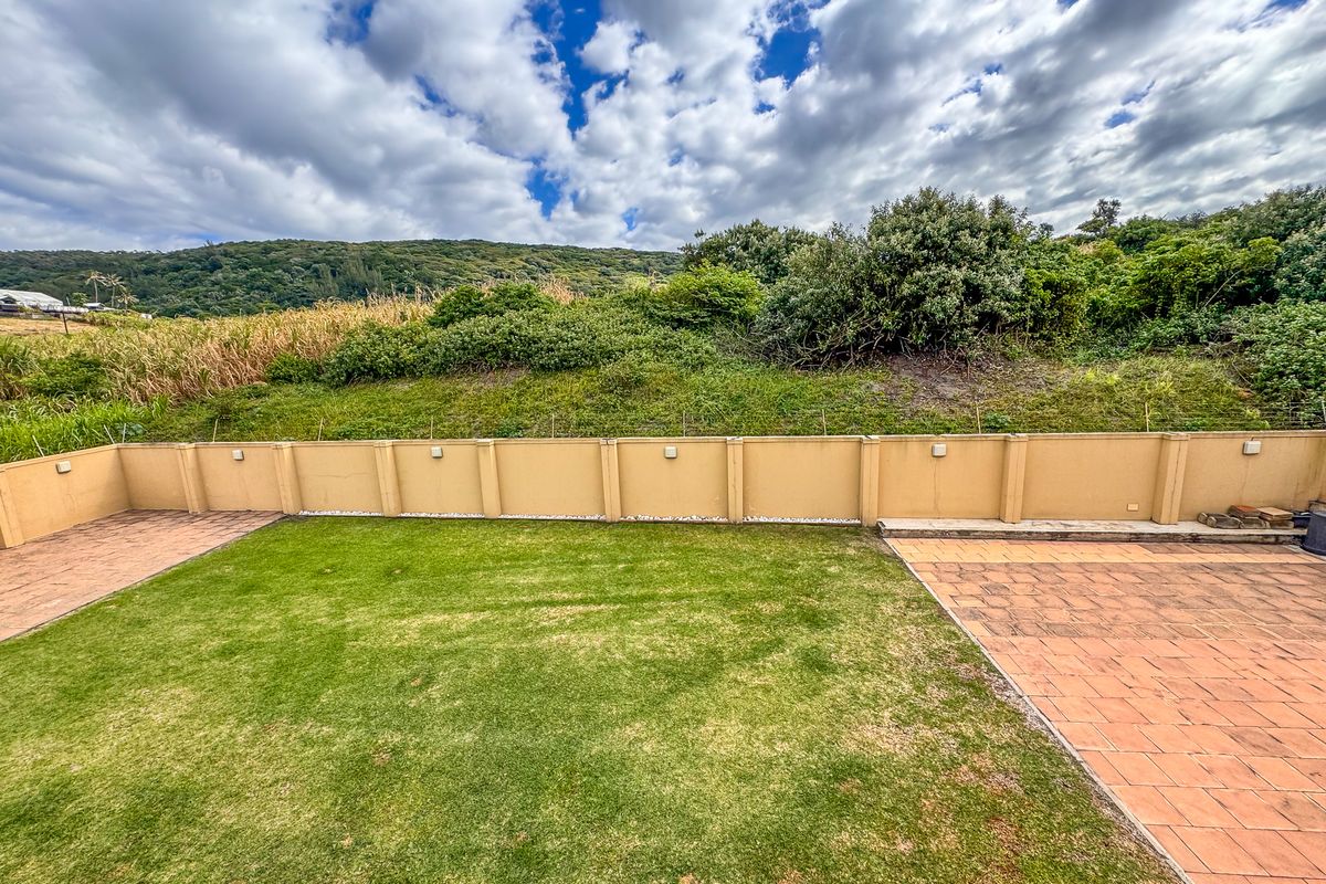 A private rear garden featuring a paved patio area, a central lawn, and a perimeter boundary wall with integrated lighting.