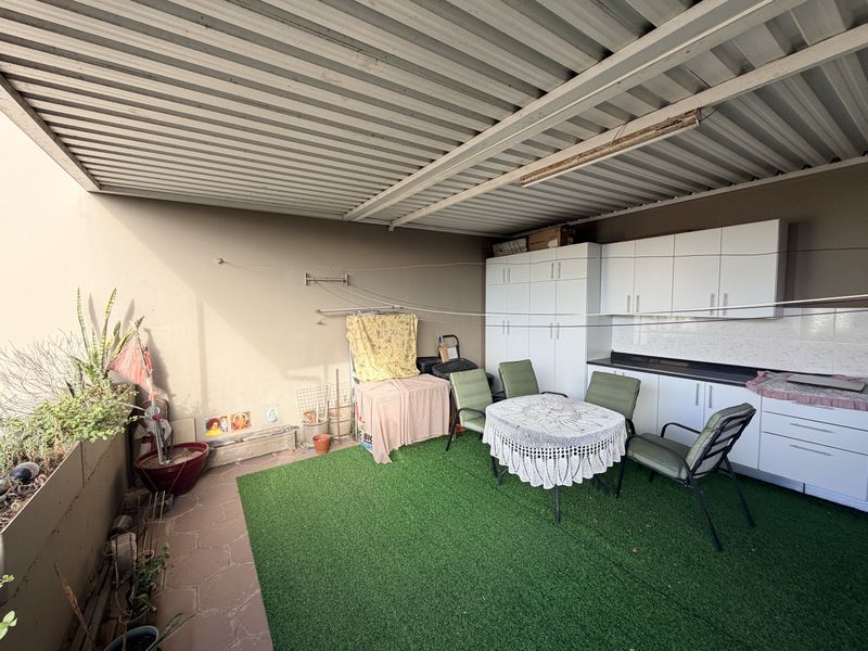 Covered patio area featuring built-in storage cabinetry, a functional countertop workspace, and artificial turf flooring, providing a versatile outdoor living and utility space.
