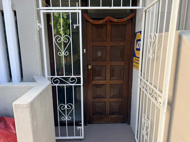 Main entrance featuring a solid timber panel door protected by a white metal security gate with tiled threshold.