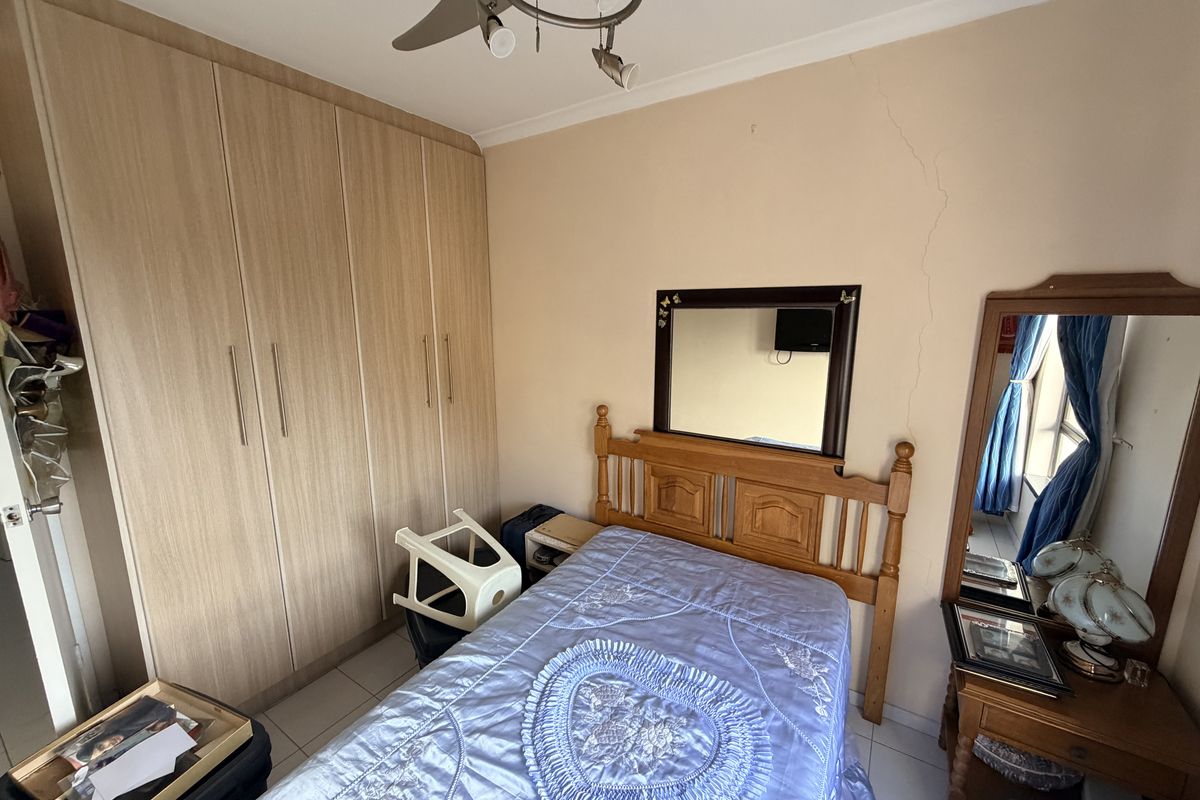 A bedroom featuring built-in wooden cupboards, tiled flooring, and a ceiling fan. The room shows signs of wear including a visible wall crack.