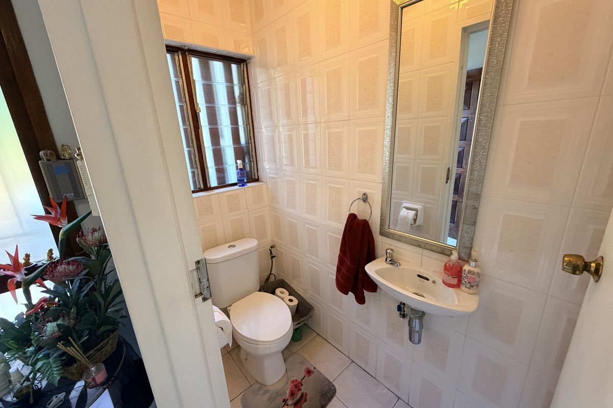 A compact guest bathroom featuring fully tiled walls and floors, a wall-mounted basin, and a standard toilet.