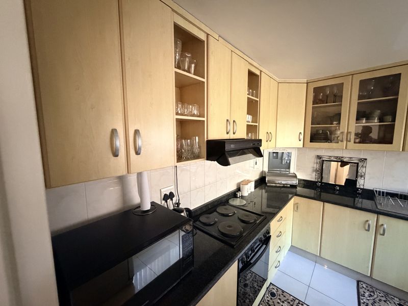 A functional kitchen featuring light wood cabinetry, black granite countertops, an electric hob, built-in oven, and tiled splashbacks.