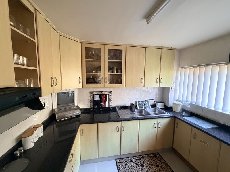 A functional kitchen featuring light wood-tone cabinetry, dark granite countertops, a double stainless steel sink, and a tiled backsplash with integrated extractor fan.