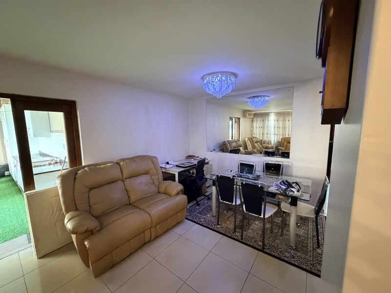 Open plan living and dining area featuring tiled flooring, a large wall mirror, and a decorative crystal chandelier, with an adjacent kitchen view.