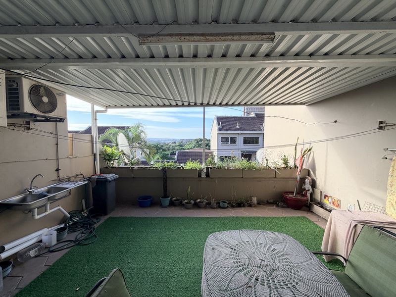 Covered patio area featuring a built-in sink, air conditioning unit, and planter boxes, offering an elevated view of the surrounding neighborhood.