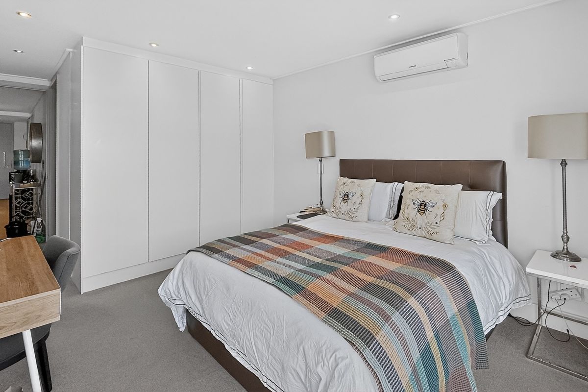 A well-maintained bedroom featuring built-in floor-to-ceiling wardrobes, recessed downlighting, and a wall-mounted air conditioning unit.