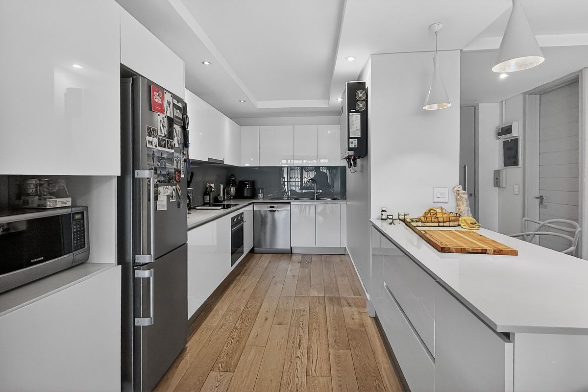 Modern kitchen featuring sleek white cabinetry, integrated appliances, a central island with breakfast bar, and warm wood-look flooring.