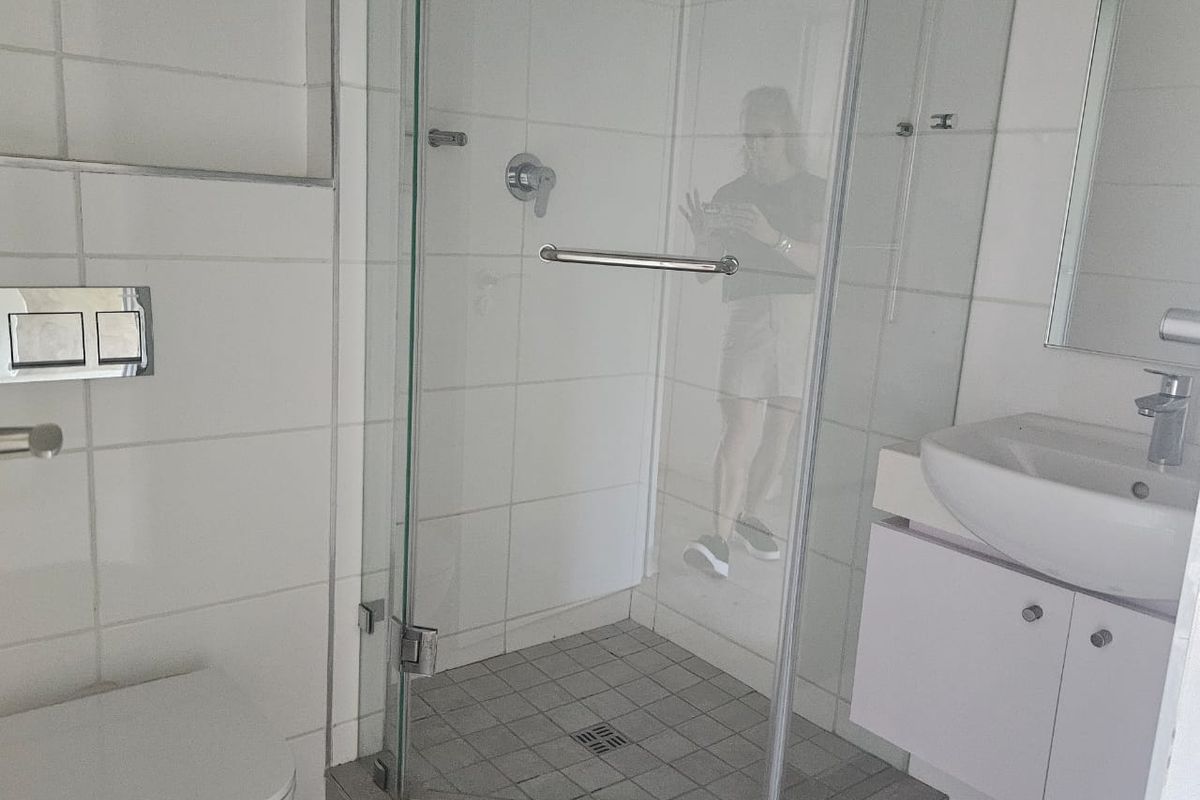 A compact bathroom featuring a glass-enclosed corner shower, wall-mounted toilet, and a vanity basin with storage cabinetry.