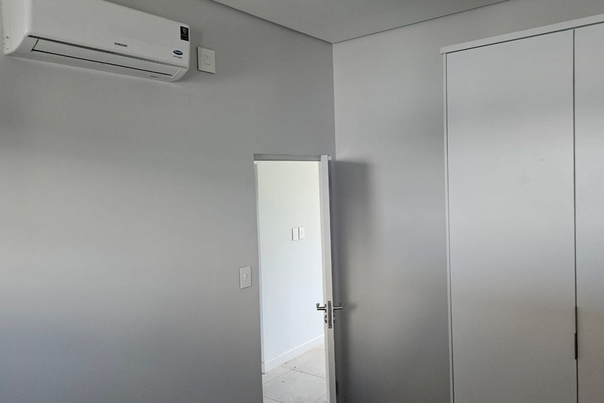 A clean bedroom interior featuring a wall-mounted air conditioning unit, built-in wardrobe, and recessed ceiling lighting.