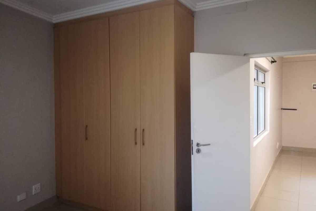 A bedroom featuring built-in wooden cupboards and tiled flooring, with an open doorway leading to an adjacent hallway.