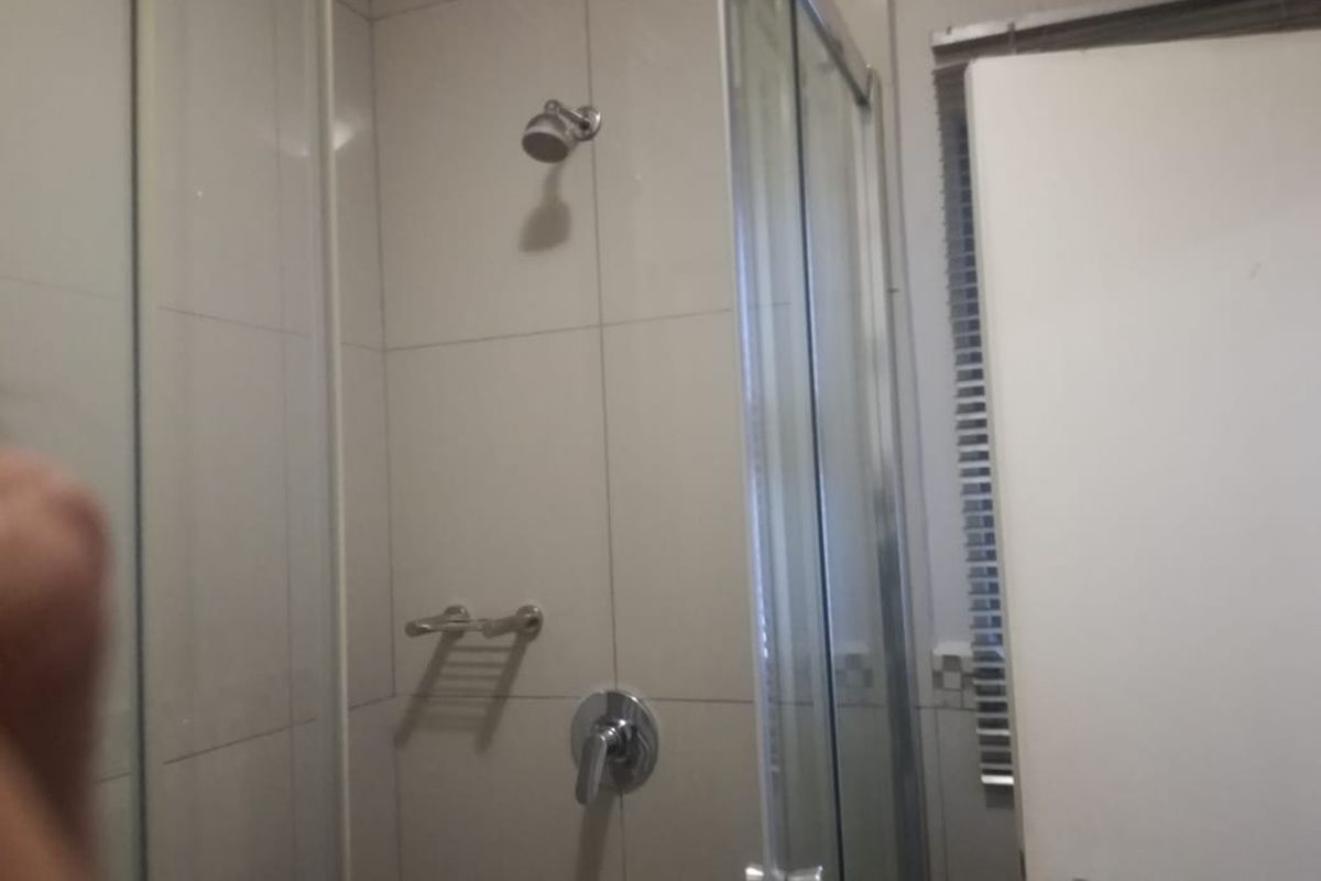 A functional shower enclosure featuring tiled walls, a glass door, and a chrome shower mixer and head.