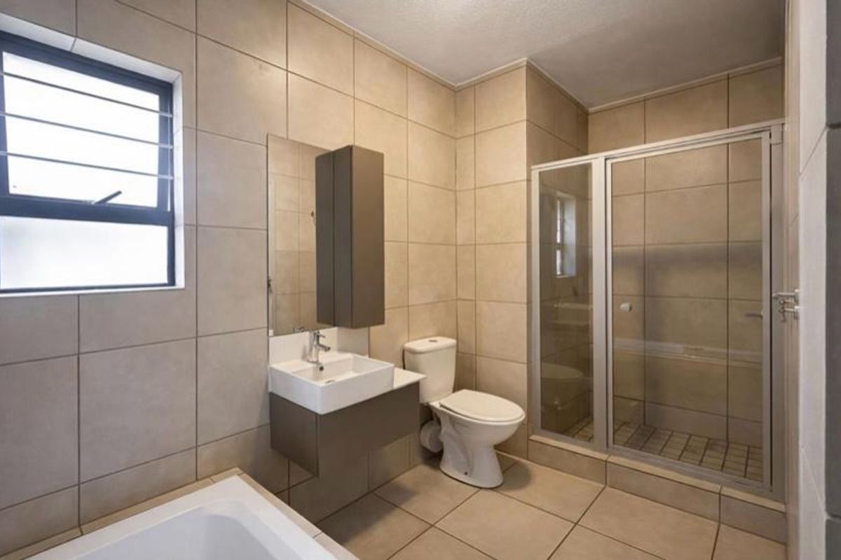 A modern bathroom featuring a glass-enclosed shower, a separate bathtub, a wall-mounted vanity with a basin, and neutral floor-to-ceiling tiling.