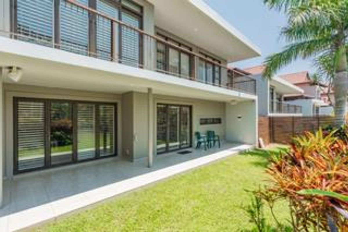 A well-maintained townhouse rear exterior featuring a covered patio, tiled flooring, and large sliding glass doors leading to a private garden area.