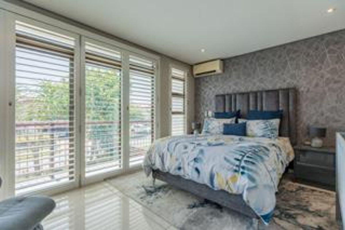 A well-appointed bedroom featuring large sliding glass doors with integrated shutters, a wall-mounted air conditioning unit, and a feature wallpaper wall.