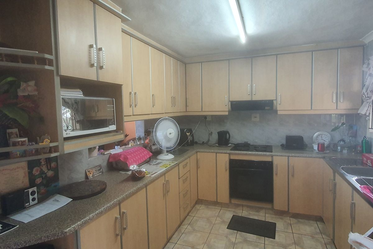 A functional kitchen featuring laminate cabinetry, built-in oven, hob, extractor fan, and a double bowl sink with tiled backsplash and flooring.