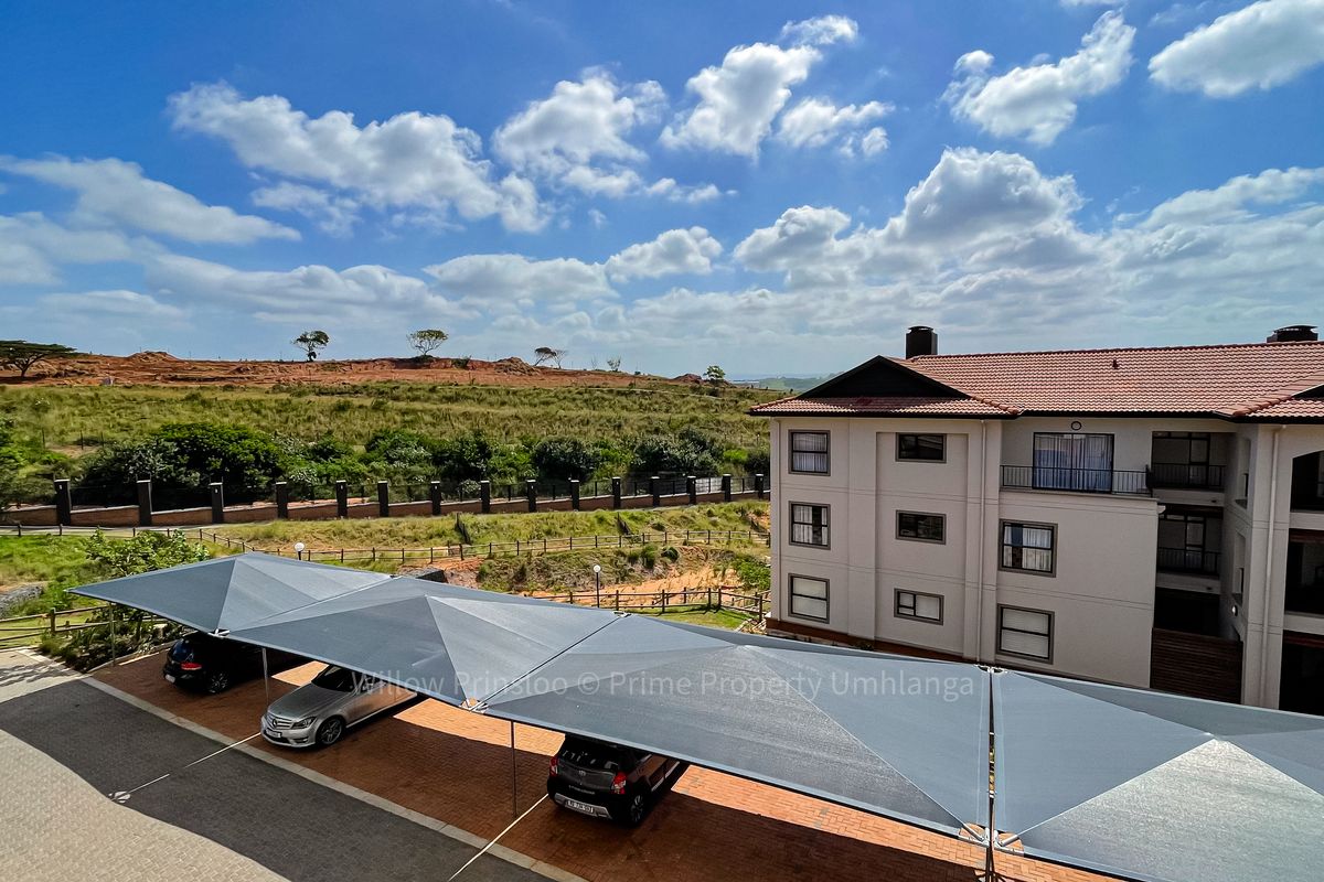 Elevated view of the apartment complex exterior, featuring covered parking bays and surrounding landscaped grounds under a clear blue sky.