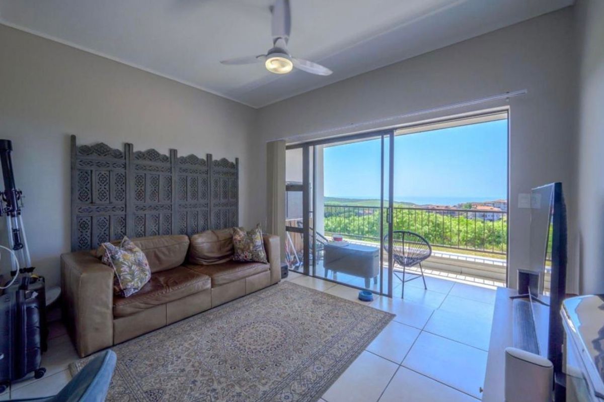 A bright living room featuring large sliding glass doors that open onto a balcony with scenic coastal and landscape views.
