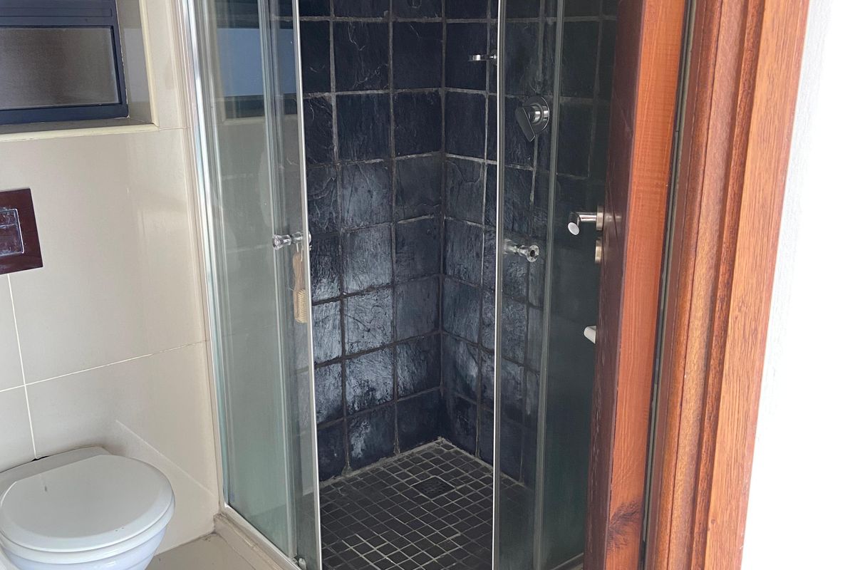 A compact bathroom featuring a corner glass shower enclosure with dark textured tiling and a wall-mounted toilet.