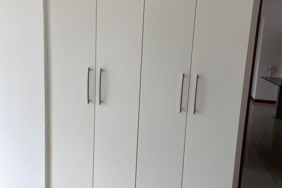 A built-in white wardrobe with modern metal handles, featuring clean lines and integrated design within the bedroom or hallway space.