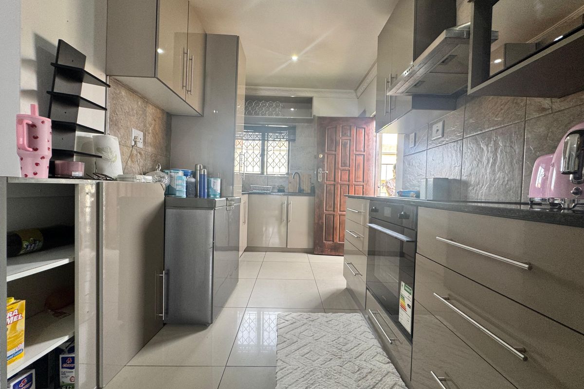 Modern galley-style kitchen featuring high-gloss cabinetry, integrated oven, extractor fan, tiled flooring, and stone-look backsplash tiles.