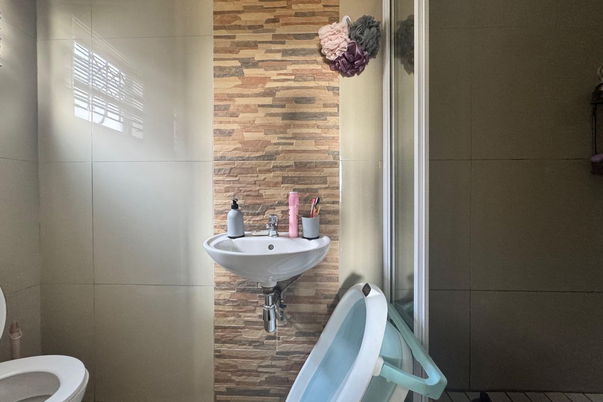 A compact bathroom featuring a wall-mounted basin with a decorative stone-look tiled feature wall, a toilet, and a shower enclosure.