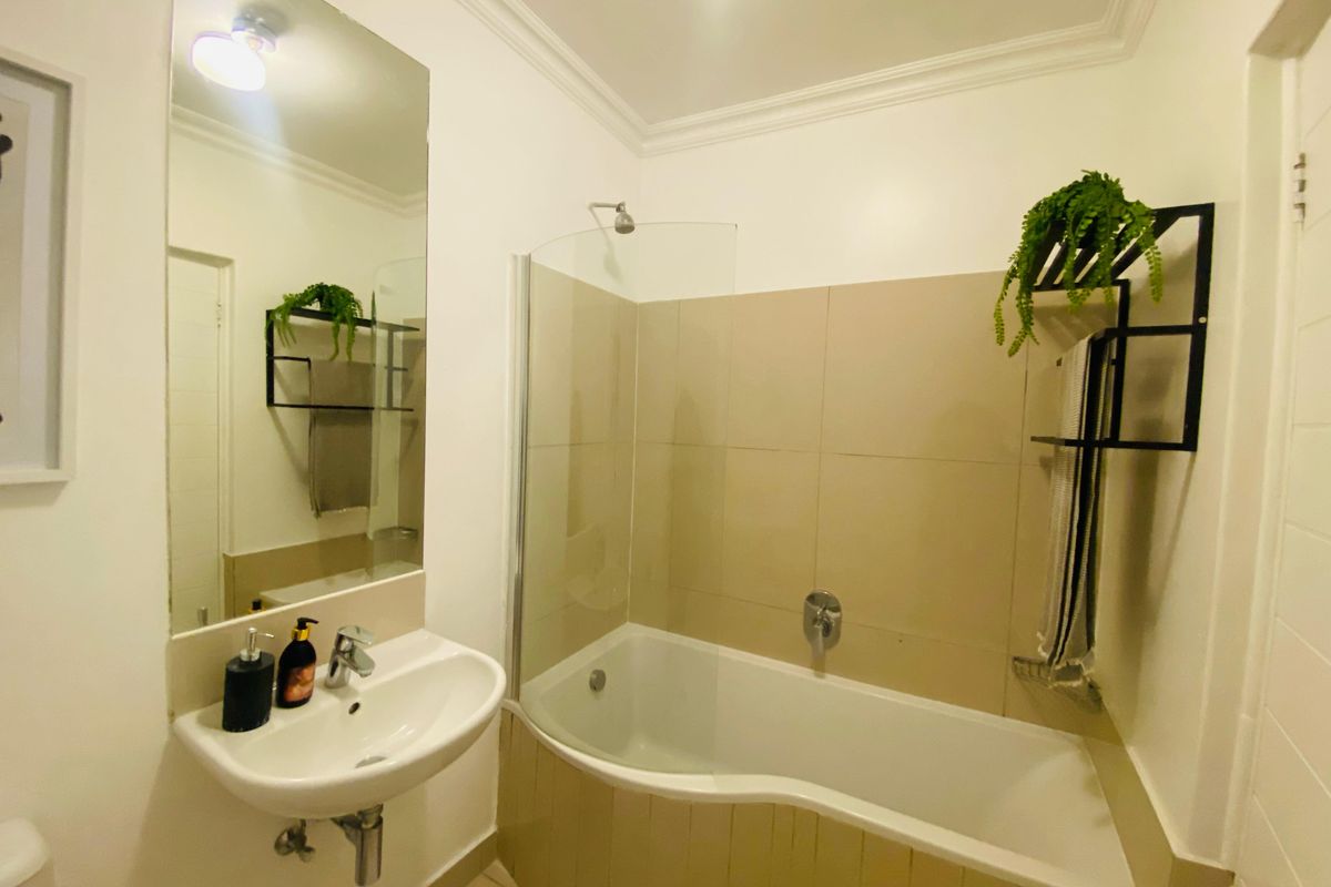 A functional bathroom featuring a wall-mounted basin, a shower-over-bath combination with a glass screen, and neutral wall tiling.
