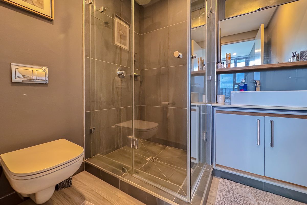 Modern bathroom featuring a glass-enclosed shower, wall-mounted toilet, and a vanity unit with a basin.