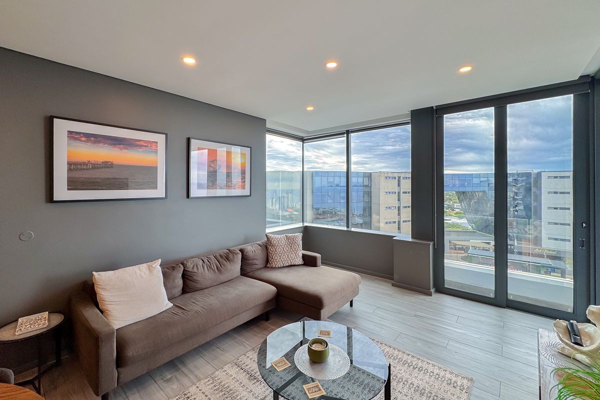 Modern living room featuring floor-to-ceiling windows, recessed lighting, and access to a private balcony with urban views.