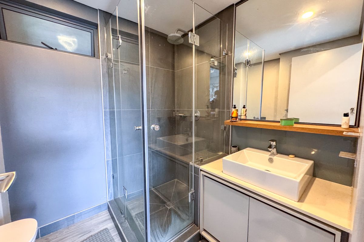 Modern bathroom featuring a glass-enclosed shower, a contemporary vessel sink with vanity storage, and a large wall-mounted mirror.