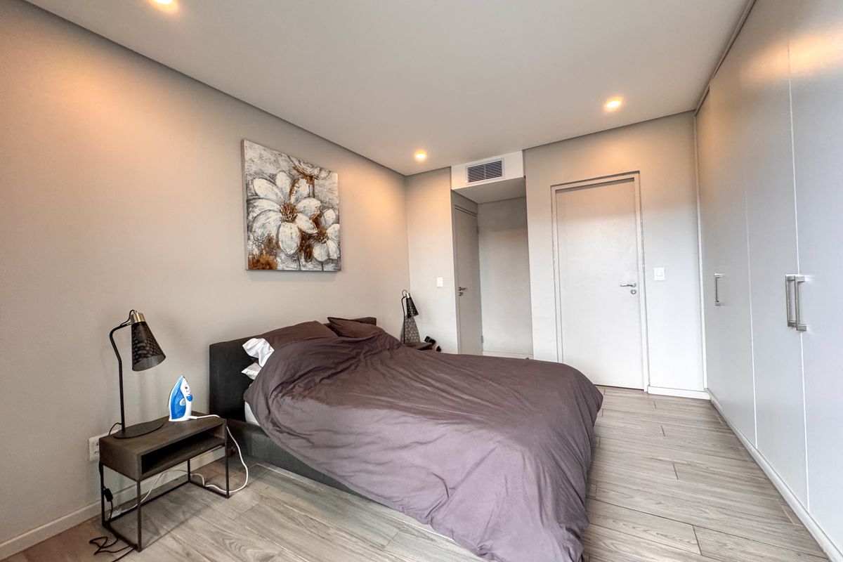 Modern bedroom featuring light wood-look flooring, recessed ceiling lighting, integrated air conditioning vent, and extensive floor-to-ceiling built-in wardrobe cabinetry.