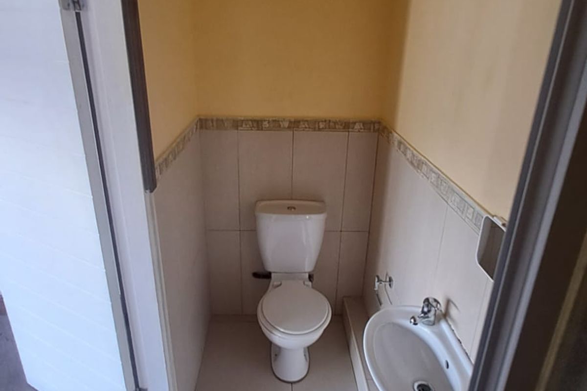 A compact guest bathroom featuring a white toilet, wall-mounted basin, tiled flooring, and half-tiled walls with a decorative border.