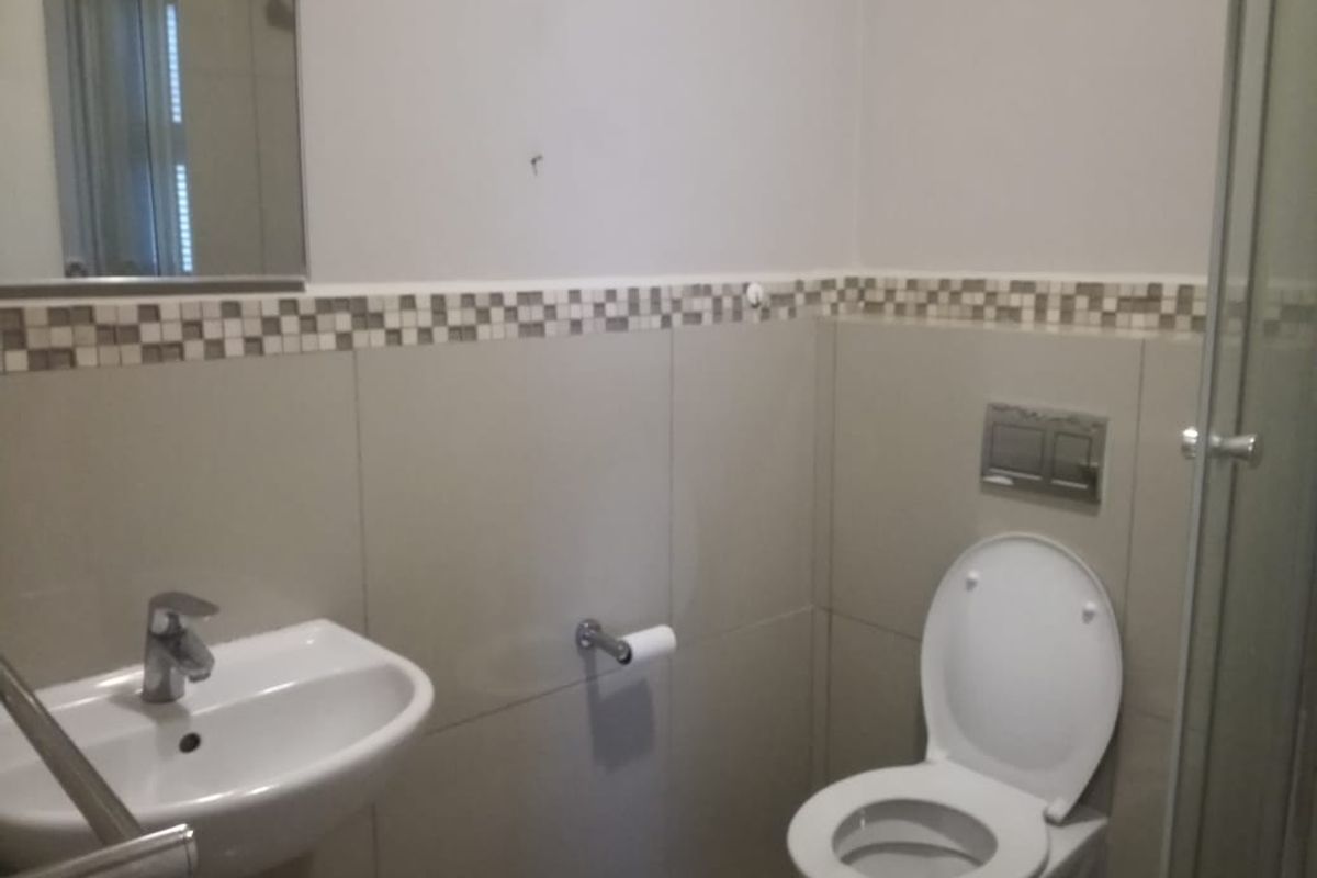 A functional bathroom featuring a wall-mounted basin, a concealed cistern toilet, and a glass shower enclosure with neutral wall tiling.