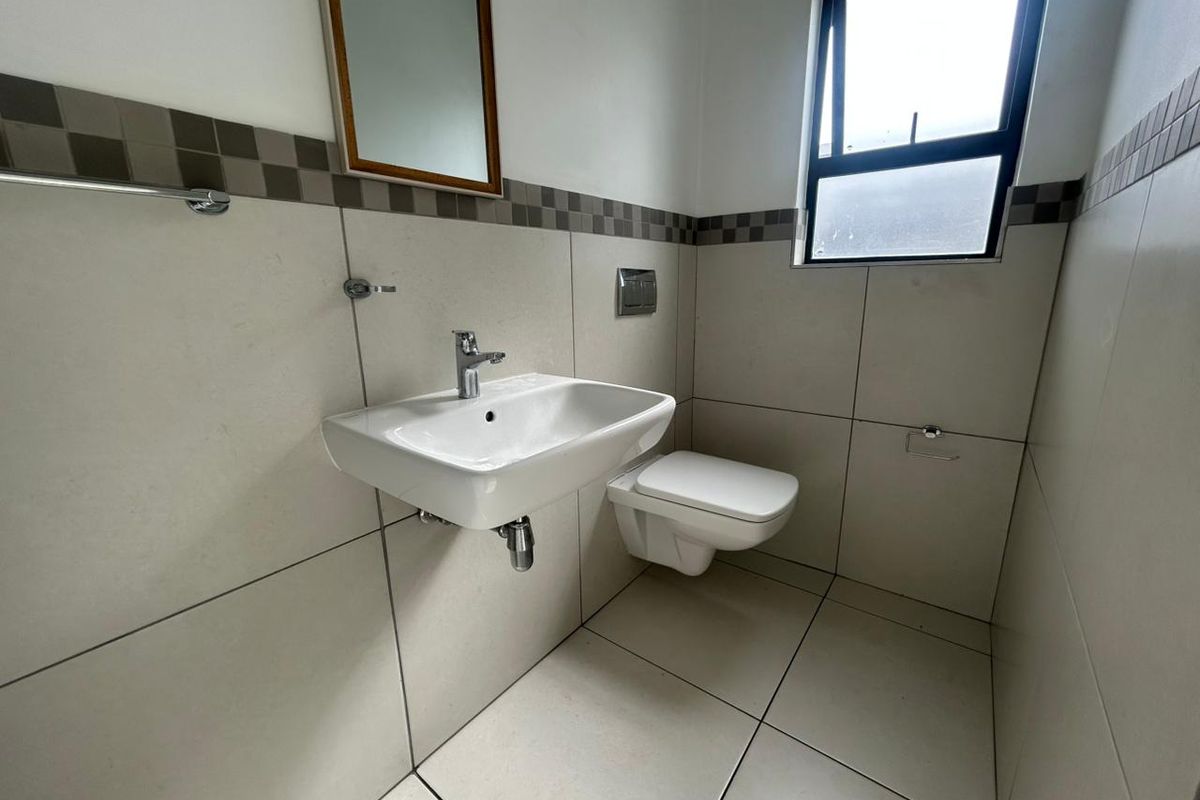 A modern bathroom featuring a wall-mounted basin, a wall-hung toilet, and neutral floor-to-ceiling tiling with a decorative border.