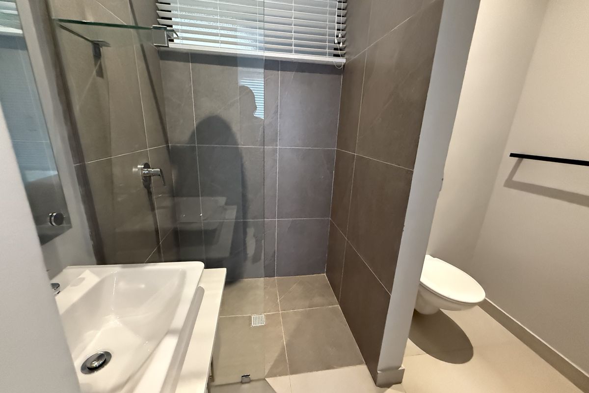 Modern bathroom featuring a walk-in shower with glass screen, wall-mounted toilet, and a sleek vanity basin with contemporary tiling.