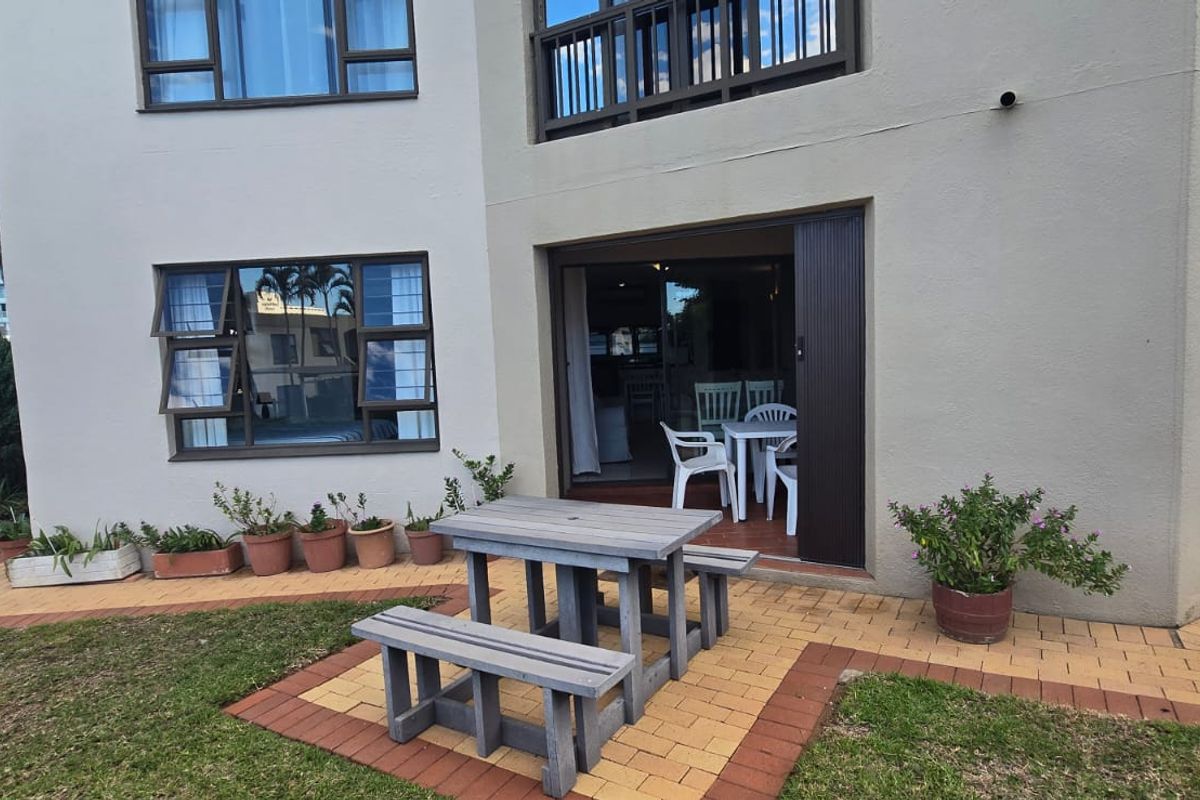 Ground floor apartment exterior featuring a paved patio area, sliding door access, and aluminum window frames, set within a landscaped residential complex.