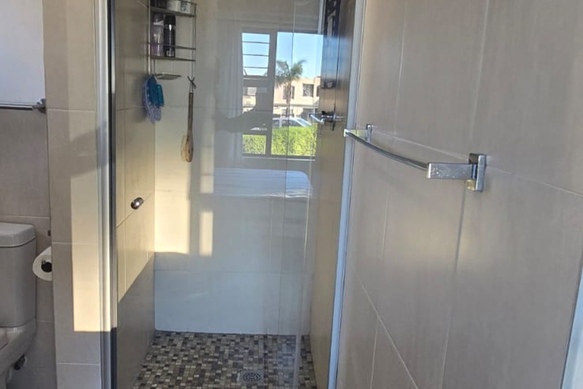 A modern bathroom featuring a glass-enclosed shower with mosaic tile flooring, neutral wall tiles, and a wall-mounted towel rail.