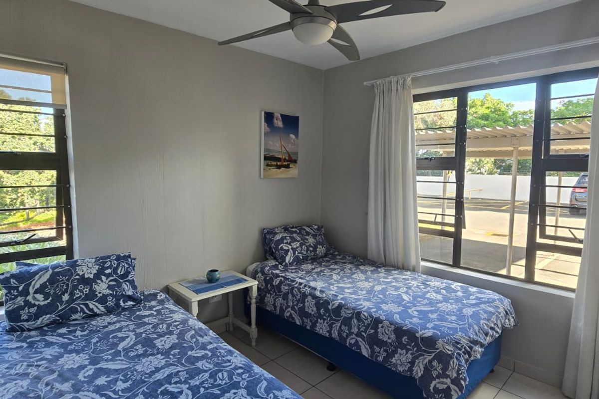 A bright bedroom featuring tiled flooring, large windows with natural light, and a ceiling fan.