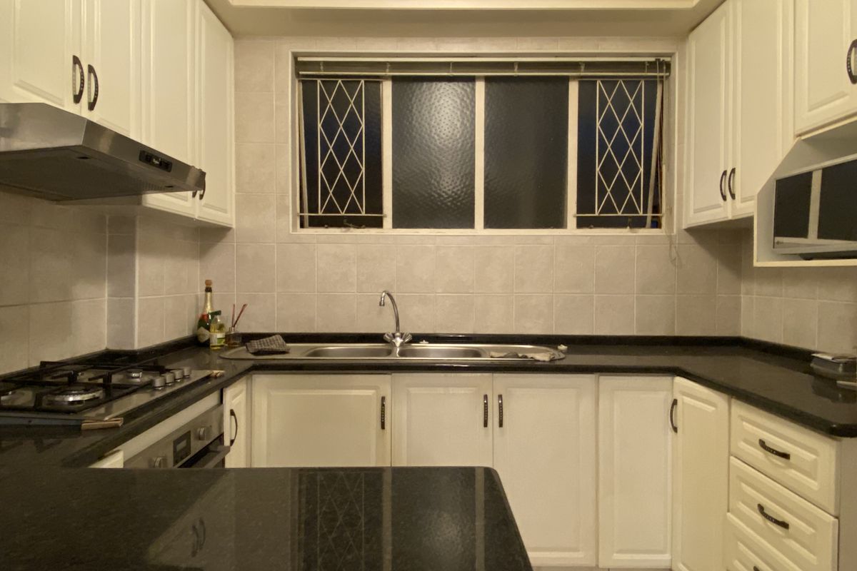 A functional kitchen featuring white cabinetry, dark granite countertops, a built-in gas hob, oven, and extractor fan with a tiled backsplash.