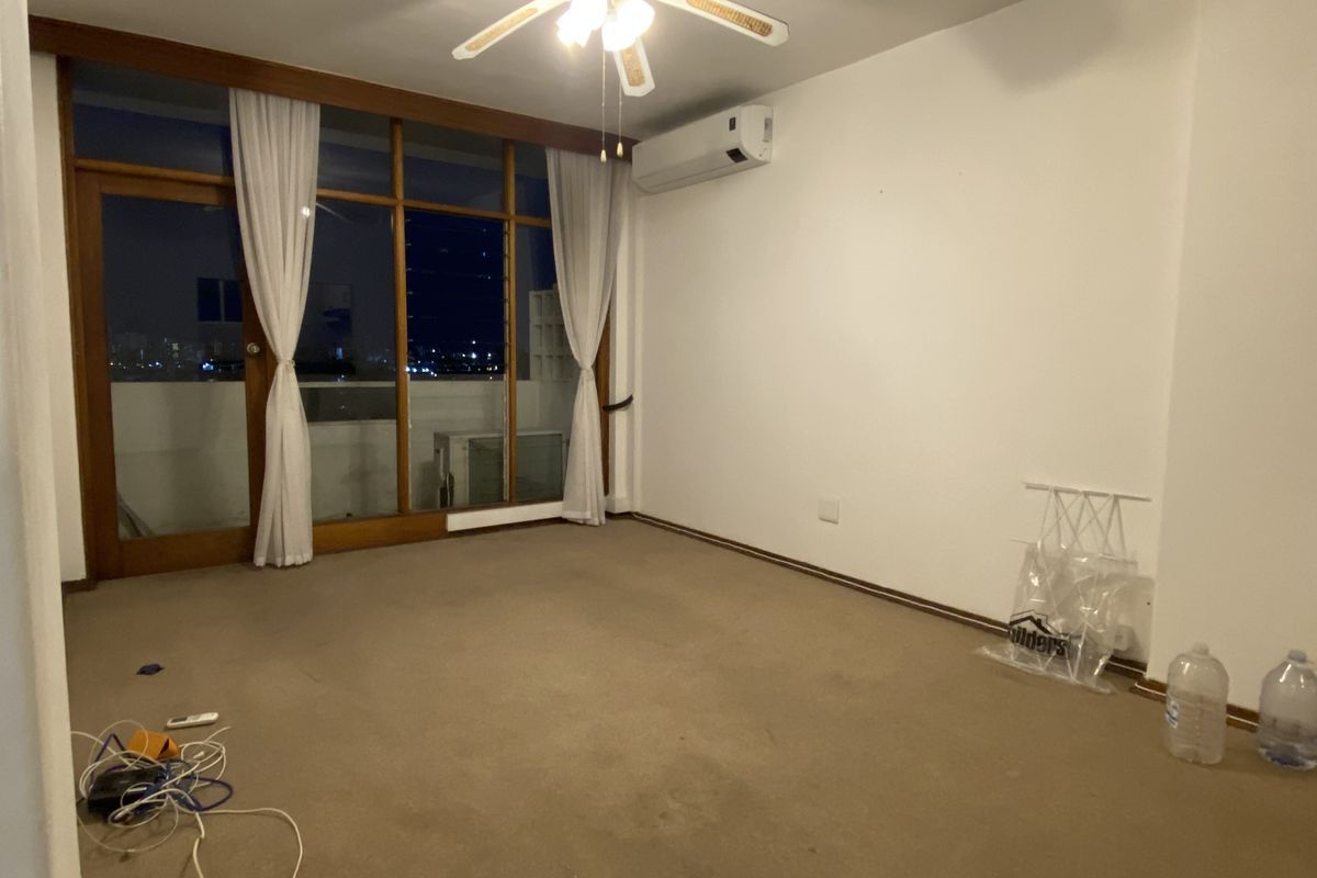 Spacious living area featuring wall-mounted air conditioning, a ceiling fan, and large floor-to-ceiling wooden framed windows providing access to an outdoor balcony.
