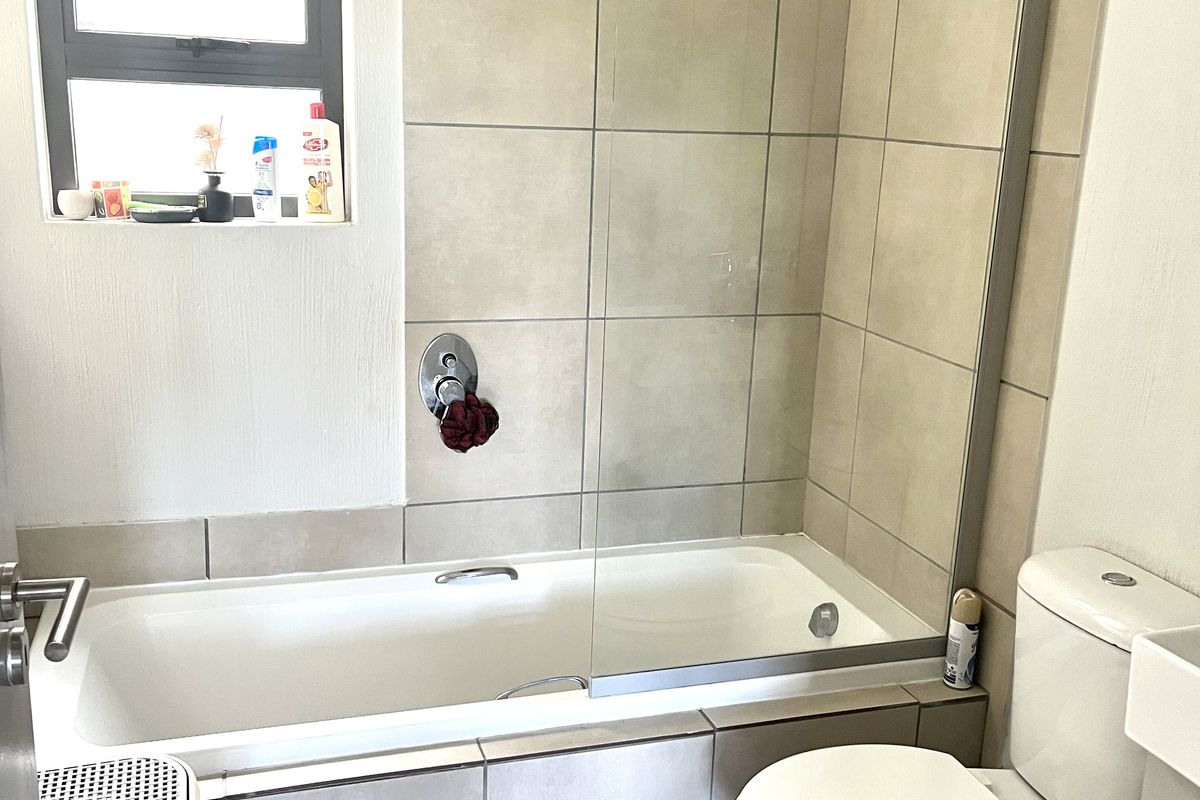 A functional bathroom featuring a combined bathtub and shower with a glass screen, neutral wall tiling, and a standard toilet.