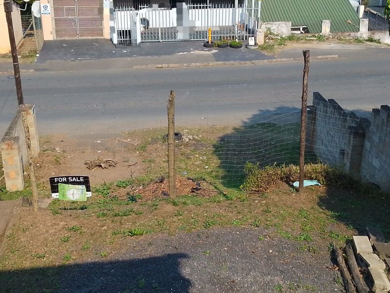 An elevated view of the front property boundary featuring a gravel driveway, concrete block walling, and wire mesh fencing in need of maintenance.