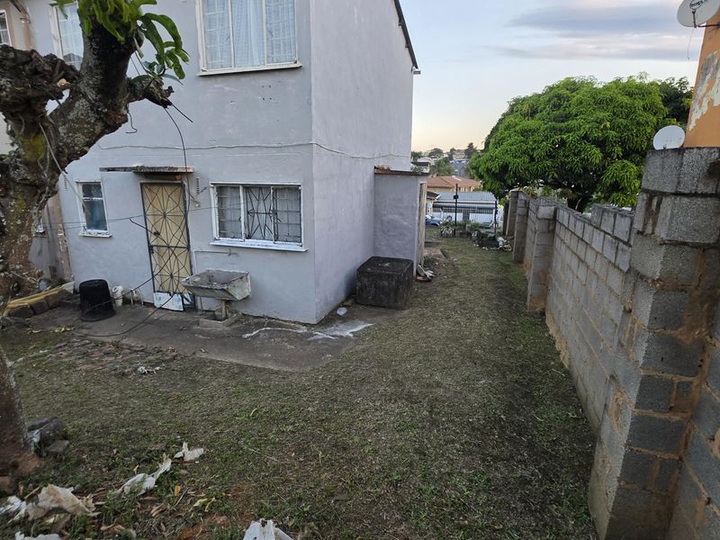 Rear exterior view of the property featuring a concrete block boundary wall, small garden area, and an external utility sink.