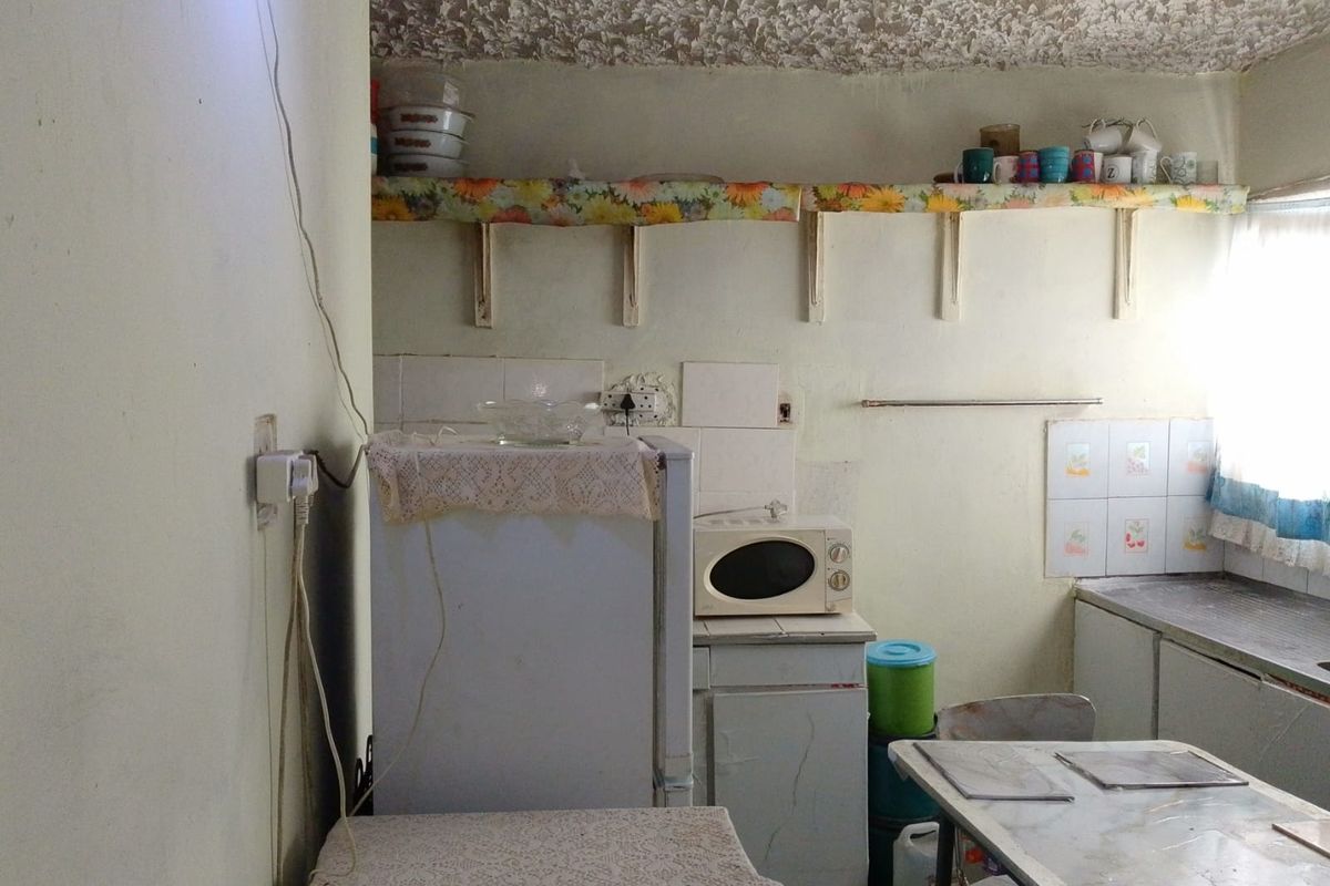 A dated kitchen area featuring basic cabinetry, tiled splashbacks, and open shelving, requiring modernization and cosmetic updates to improve functionality and aesthetic appeal.