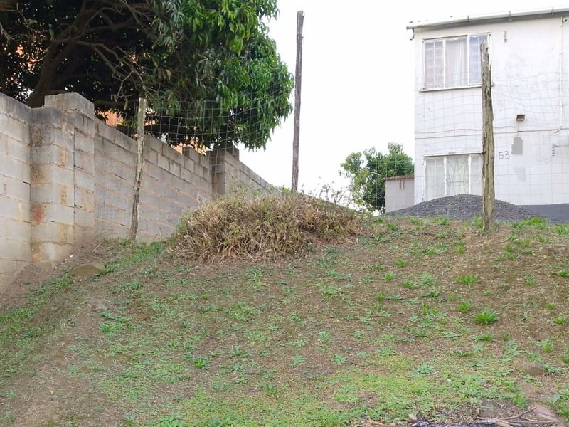 Rear exterior view of the property featuring a sloped garden area, concrete block boundary wall, and wire mesh fencing.