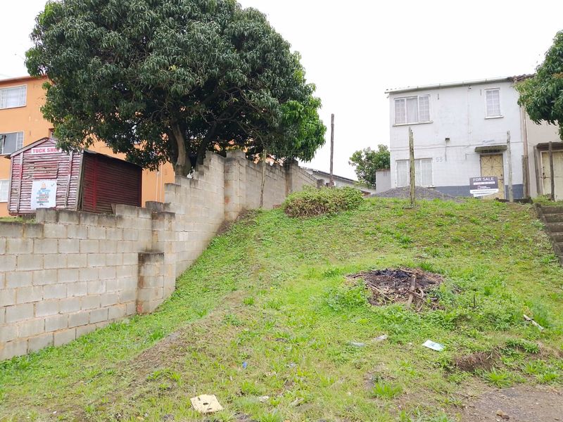 Front view of a residential property featuring a sloped garden, concrete boundary wall, and access stairs leading to the main building.