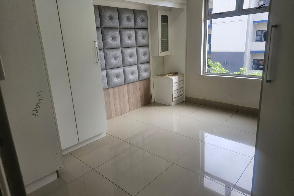 A bedroom featuring built-in white cabinetry, integrated storage units, a padded headboard panel, and tiled flooring with natural light from the window.
