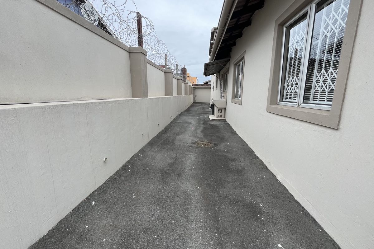 A narrow side passage of the property featuring a paved walkway, perimeter boundary wall with security wire, and an external utility sink.