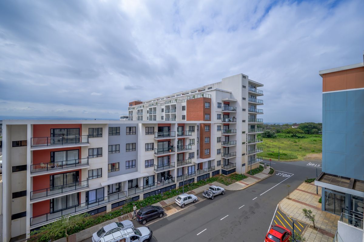 An elevated exterior view of the Summer Ridge apartment complex, showcasing its modern multi-story facade, balconies, and surrounding street infrastructure.
