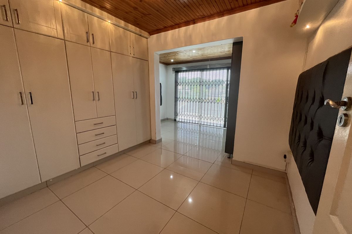 A bedroom featuring extensive built-in cabinetry, tiled flooring, and a timber-clad ceiling, leading to a secondary space with a security gate.